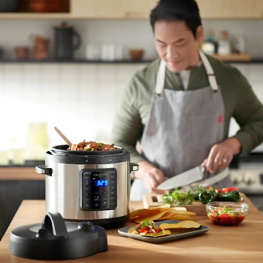 A chef wearing an apron cooking in the kitchen, using a smart slow cooker device in the foreground.