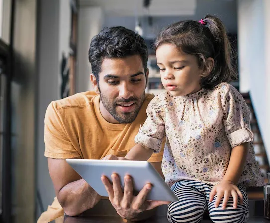 Un padre le muestra a su hija pequeña cómo usar una tablet
